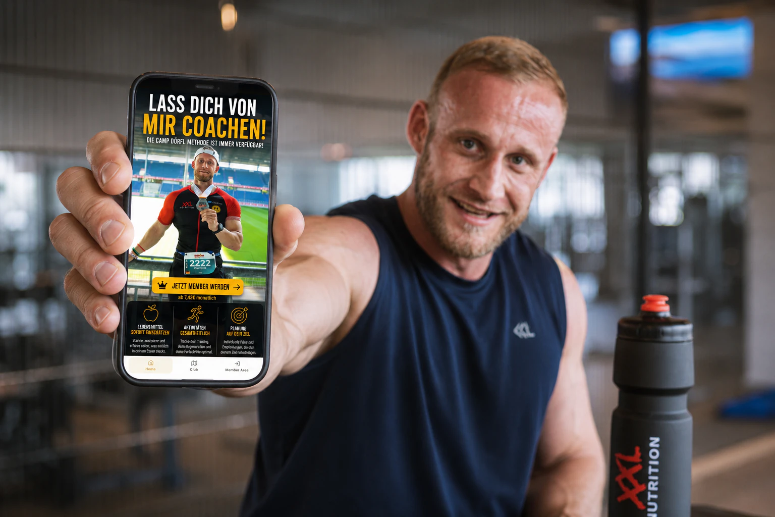Dominik Dörfl zeigt die Camp Dörfl App auf einem Smartphone im Fitnessstudio