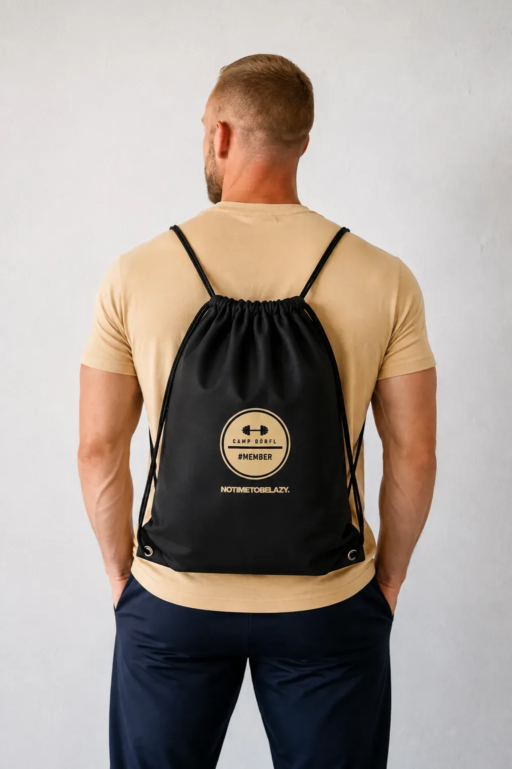Camp Dörfl bag, a black drawstring bag with a gold #MEMBER emblem, worn on the back